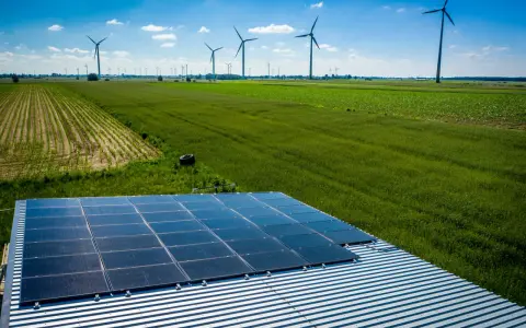 Panele słoneczne na dachu i wiatraki na polu, symbolizujące program agroenergia i zrównoważony rozwój.