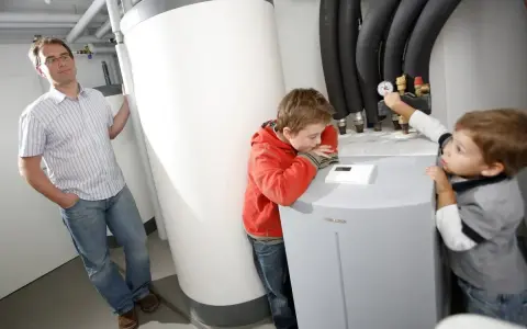 Ojciec z dziećmi przy pompie ciepła. Czy pompę ciepła można wyłączyć? Chłopcy badają urządzenie, ojciec obserwuje.