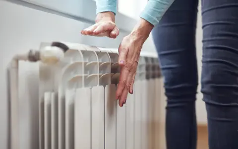 Dłonie sprawdzają temperaturę grzejnika, zastanawiając się, dlaczego grzejnik jest zimny na dole.