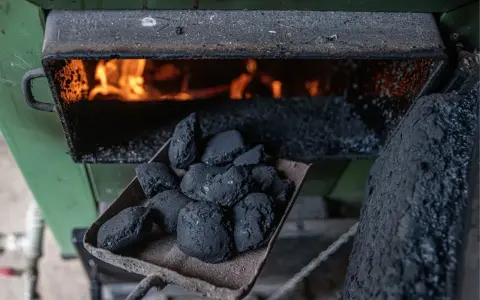 Łopata z węglem brunatnym czeka na załadunek do pieca węglowego. W palenisku żarzą się płomienie, gotowe do ogrzania domu.