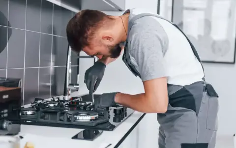 Fachowiec w rękawiczkach dokonuje wymiany kuchenki gazowej w bloku, naprawiając ją precyzyjnie.