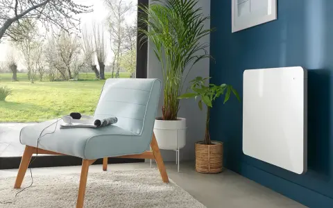 Nowoczesny, biały grzejnik elektryczny na granatowej ścianie. Idealny jako jaki grzejnik do pokoju 10m2, obok jasnoniebieskiej kanapy i roślin.