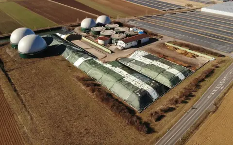 Duże, białe kopuły i zielone, zakryte pryzmy na terenie biogazowni. Czy biogazownia śmierdzi? Zależy od wiatru i odległości.