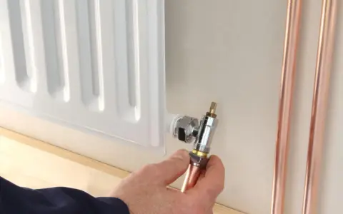 Instalator pokazuje, jak odkręcić dolny zawór grzejnika, trzymając miedzianą rurkę.