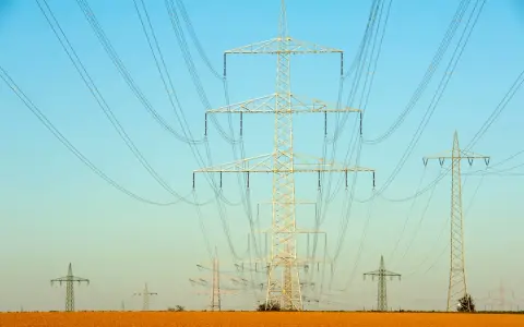 Linie energetyczne przecinają błękitne niebo. Czy ta sieć przesyłowa 1MW ile to kw zasila okoliczne pola?