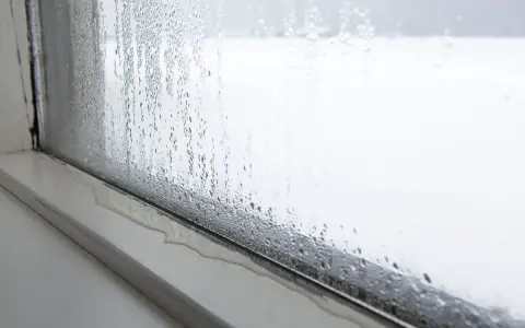 Kondensacja na oknie. Krople wody spływają po szybie, tworząc kałużę na parapecie. To zjawisko, kondensacja, pokazuje różnicę temperatur.