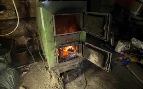 Zielony piec z otwartymi drzwiczkami, w którym pali się ogień. Pytanie o kotły klasy 1 do kiedy jest ważne dla ogrzewania domu.