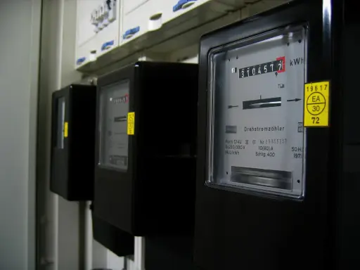 Trzy czarne liczniki energii elektrycznej z cyfrowymi wyświetlaczami i żółtymi naklejkami.