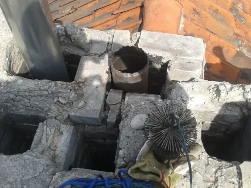Widok na komin z widocznym metalowym czopuchem i szczotką do czyszczenia. Prawidłowe podłączenie czopucha do komina jest kluczowe dla bezpieczeństwa.