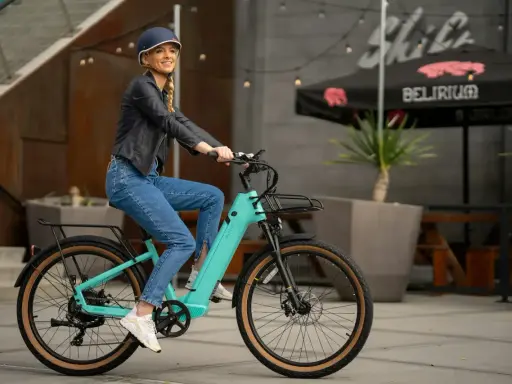 Uśmiechnięta kobieta na turkusowym rowerze elektrycznym. Idealny sposób na skorzystanie z dofinansowania do zakupu roweru elektrycznego i odkrywanie miasta.