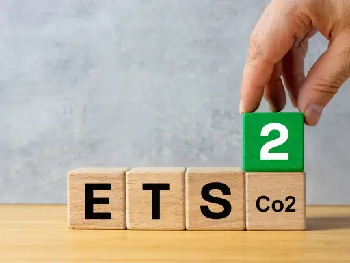 Dłoń układa kostkę z cyfrą 2 na kostce z napisem "CO2", obok kostek z napisami "ETS". Sugeruje to nowy podatek od ogrzewania gazem.