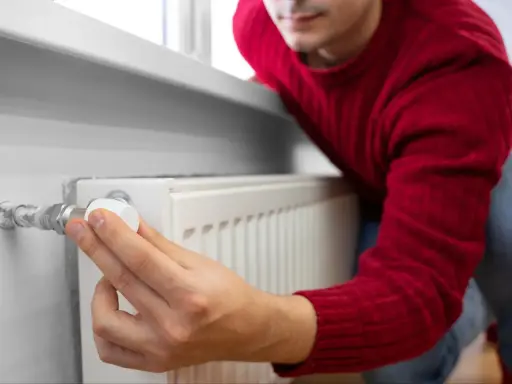 Mężczyzna w czerwonym swetrze reguluje termostat grzejnika. Dobry doradca energetyczny pomoże Ci oszczędzać ciepło.