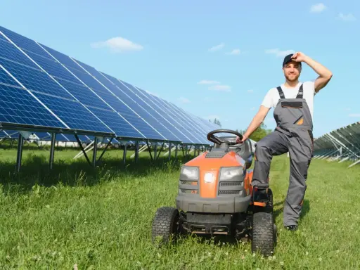 Rolnik w ogrodniczkach odpoczywa przy traktorku, obok rzędy paneli słonecznych zapewniających czystą energię dla wsi.