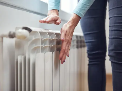 Dłonie sprawdzają temperaturę grzejnika, zastanawiając się, dlaczego grzejnik jest zimny na dole.