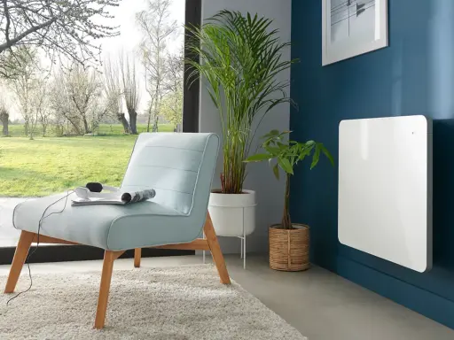 Nowoczesny, biały grzejnik elektryczny na granatowej ścianie. Idealny jako jaki grzejnik do pokoju 10m2, obok jasnoniebieskiej kanapy i roślin.