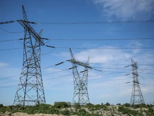 Wysokie wieże energetyczne z przewodami na tle błękitnego nieba z chmurami.