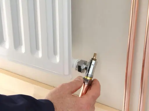 Instalator pokazuje, jak odkręcić dolny zawór grzejnika, trzymając miedzianą rurkę.