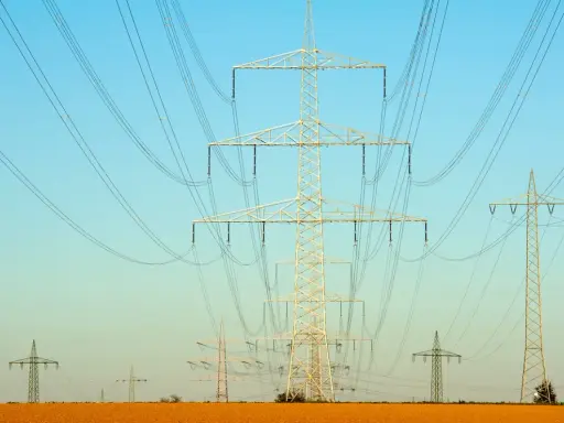 Linie energetyczne przecinają błękitne niebo. Czy ta sieć przesyłowa 1MW ile to kw zasila okoliczne pola?