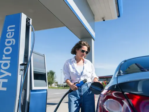 Kobieta tankuje auta na wodór. Stacja z napisem "Hydrogen" i niebieska dystrybutor.
