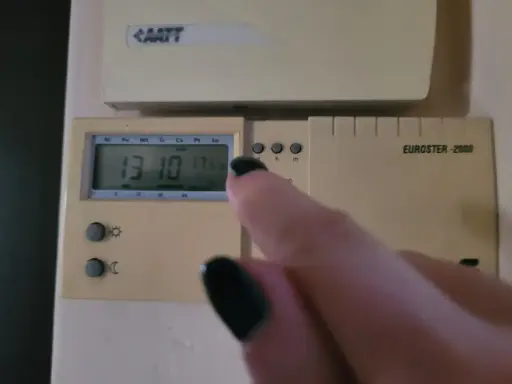 Dłoń z czarnym lakierem na paznokciach dotyka termostatu, sterowanie piecem gazowym. Na wyświetlaczu 13:10 i 17.5°C.