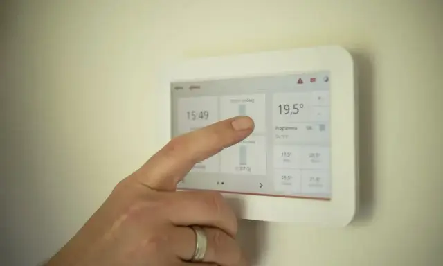 Dłoń dotyka ekranu termostatu, pokazując temperaturę 19,5°C. Ustawienia ogrzewania pomogą określić, jak często powinien włączyć się piec gazowy.