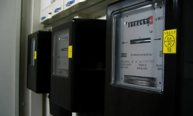Trzy czarne liczniki energii elektrycznej z cyfrowymi wyświetlaczami i żółtymi naklejkami.