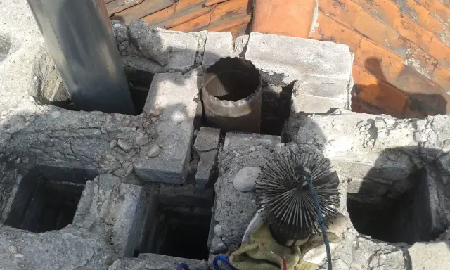 Widok na komin z widocznym metalowym czopuchem i szczotką do czyszczenia. Prawidłowe podłączenie czopucha do komina jest kluczowe dla bezpieczeństwa.