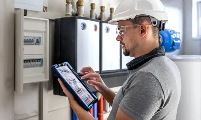 Technik w kasku i okularach ochronnych sprawdza dane na tablecie, który pokazuje schemat inteligentnego licznika.