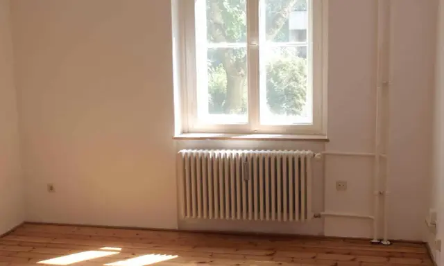 Jasne, oto opis:

Drewniana podłoga, biały grzejnik i parapet nad nim. Za oknem widać drzewa.
