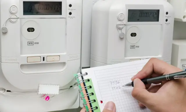 Osoba notuje odczyty liczników energii elektrycznej, przygotowując się do rozliczenia opłaty za przesył prądu.
