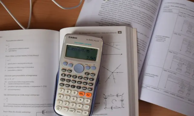 Kalkulator Casio z wyświetlonym wynikiem 2.565, obok otwarta książka z fizyki, gdzie można znaleźć informacje o tym, ile to jest kilowat i jak przeliczyć jednostki.