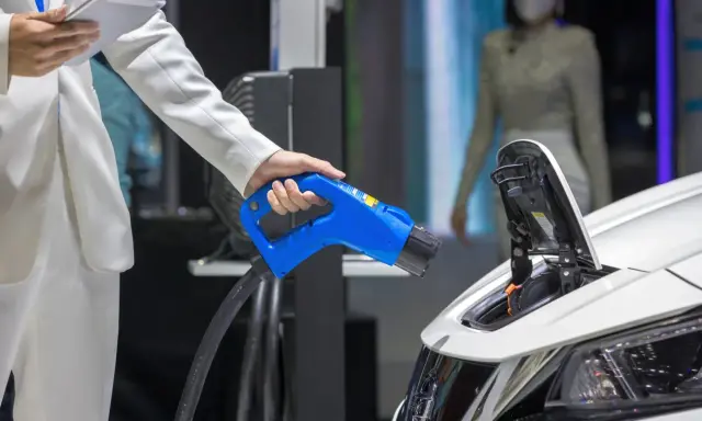 Elektromobilność w zamówieniach publicznych: ładowanie pojazdu elektrycznego. Dłoń trzymająca niebieską wtyczkę ładowarki.