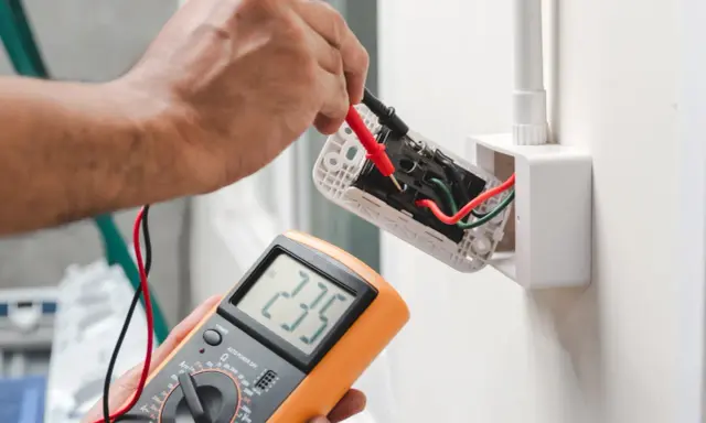 Elektryk sprawdza napięcie w gniazdku za pomocą multimetru, pokazując jak liczyć punkt elektryczny.