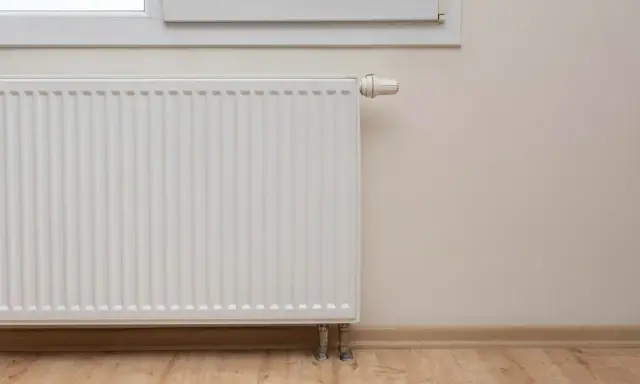 Biały grzejnik przy oknie, termostat ustawiony na minimum. Piec nie podaje ciepła na grzejniki, co oznacza zimne mieszkanie.