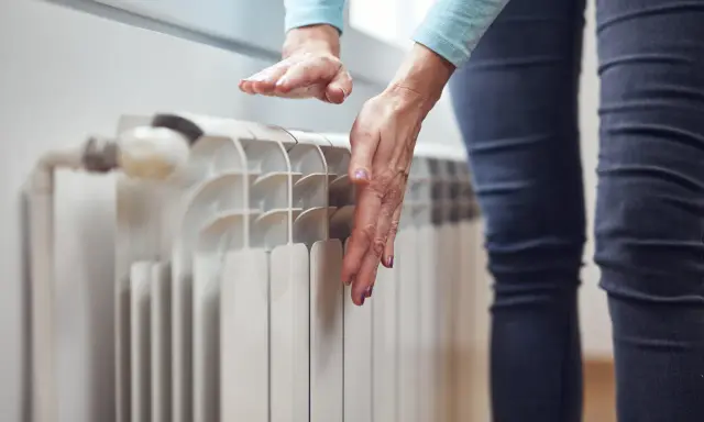 Dłonie sprawdzają temperaturę grzejnika, zastanawiając się, dlaczego grzejnik jest zimny na dole.