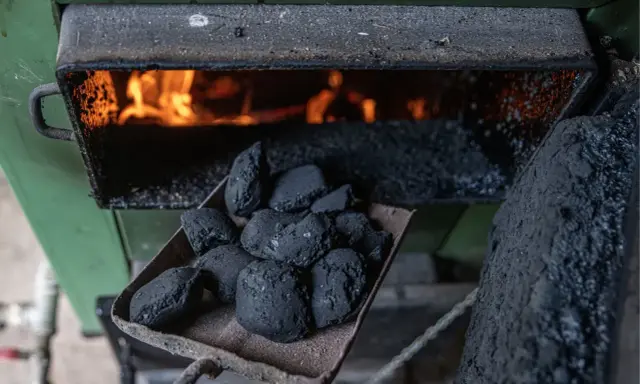 Łopata z węglem brunatnym czeka na załadunek do pieca węglowego. W palenisku żarzą się płomienie, gotowe do ogrzania domu.