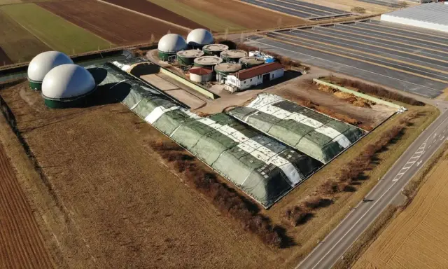 Duże, białe kopuły i zielone, zakryte pryzmy na terenie biogazowni. Czy biogazownia śmierdzi? Zależy od wiatru i odległości.