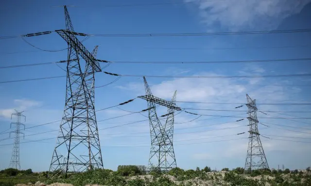 Wysokie wieże energetyczne z przewodami na tle błękitnego nieba z chmurami.
