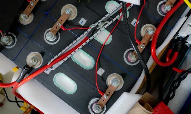 Zestaw ogniw tworzących baterię do samochodu elektrycznego, połączonych miedzianymi listwami i przewodami.