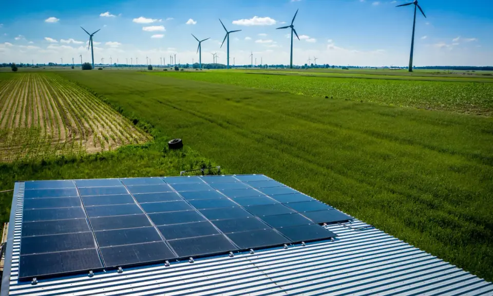 Panele słoneczne na dachu i wiatraki na polu, symbolizujące program agroenergia i zrównoważony rozwój.