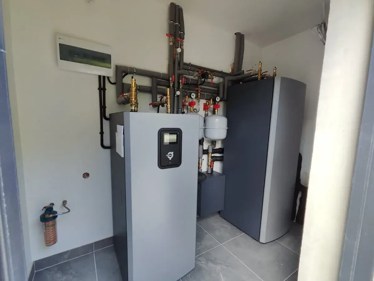 Profesjonalny montaż pompy ciepła. Widoczny zbiornik, instalacja hydrauliczna i rozdzielnica elektryczna.