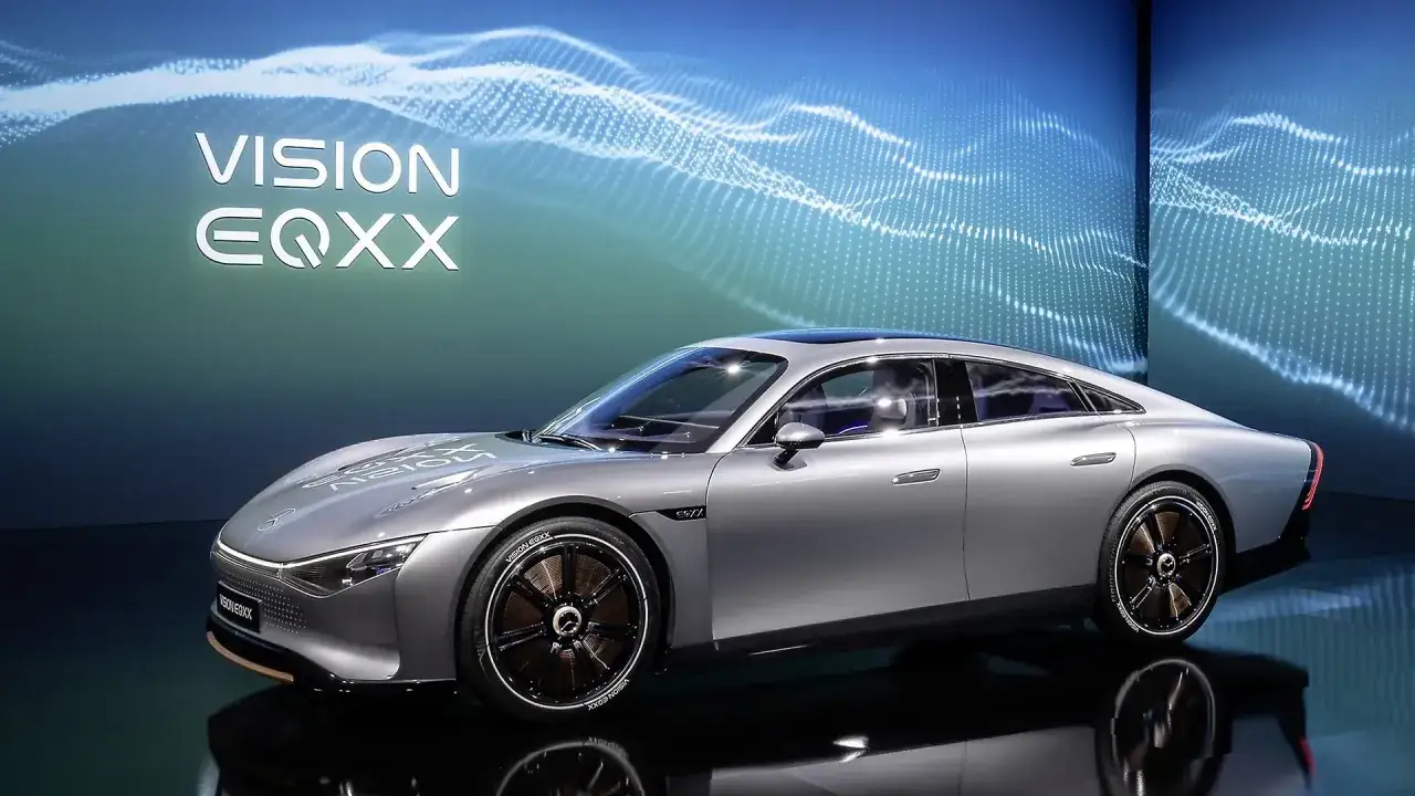 Srebrny, futurystyczny samochód elektryczny Vision EQXX, który obiecuje zasięg 1000 km, prezentowany na tle niebieskiej, falującej grafiki.