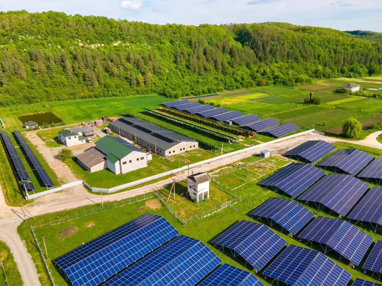 Duża farma fotowoltaiczna, gdzie panele oze rentier czerpią energię ze słońca, otoczona zielonymi wzgórzami i polami.