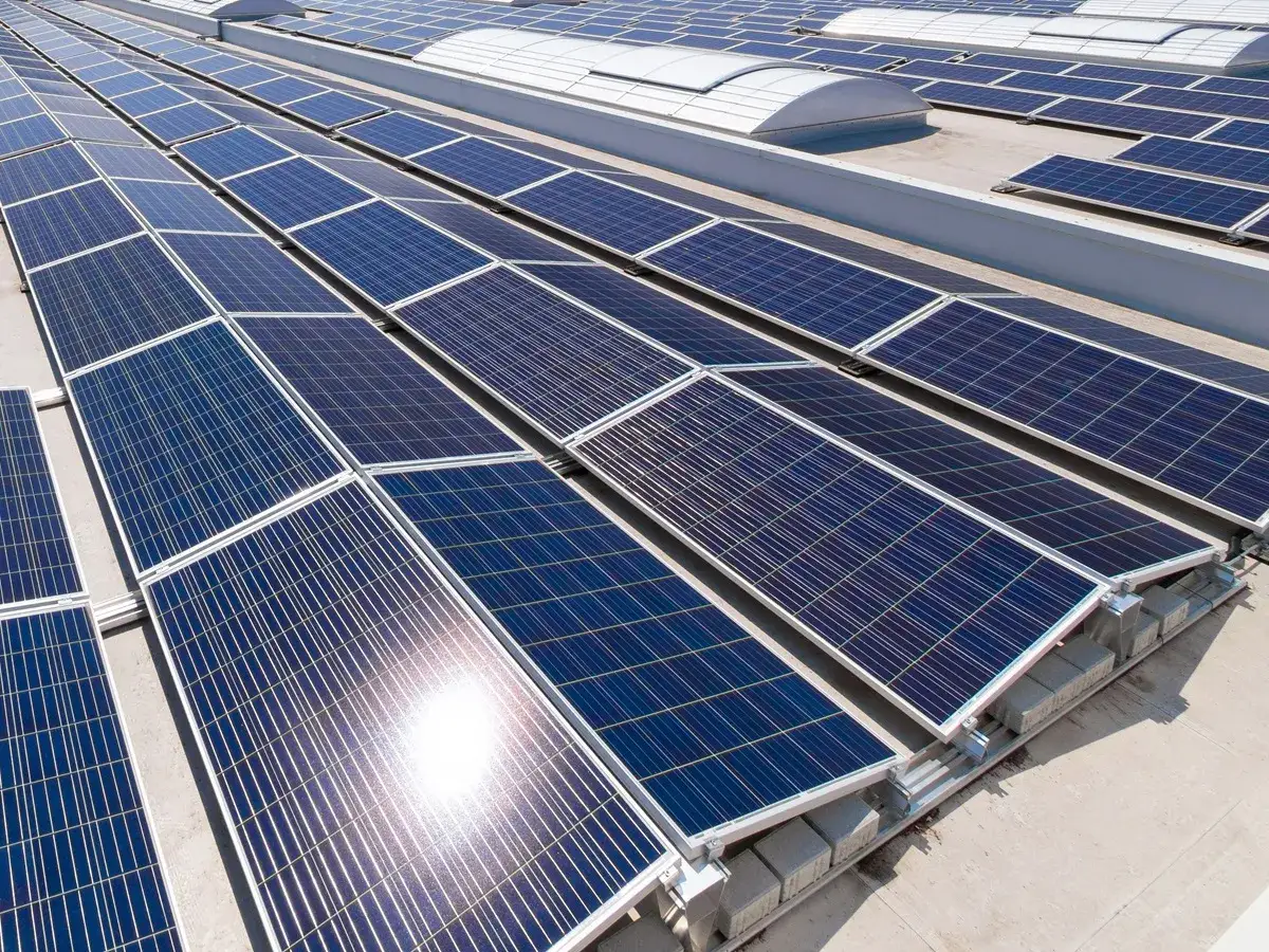 Panele fotowoltaiczne na dachu, część projektu Energia Plus. Słońce odbija się od błyszczącej powierzchni.