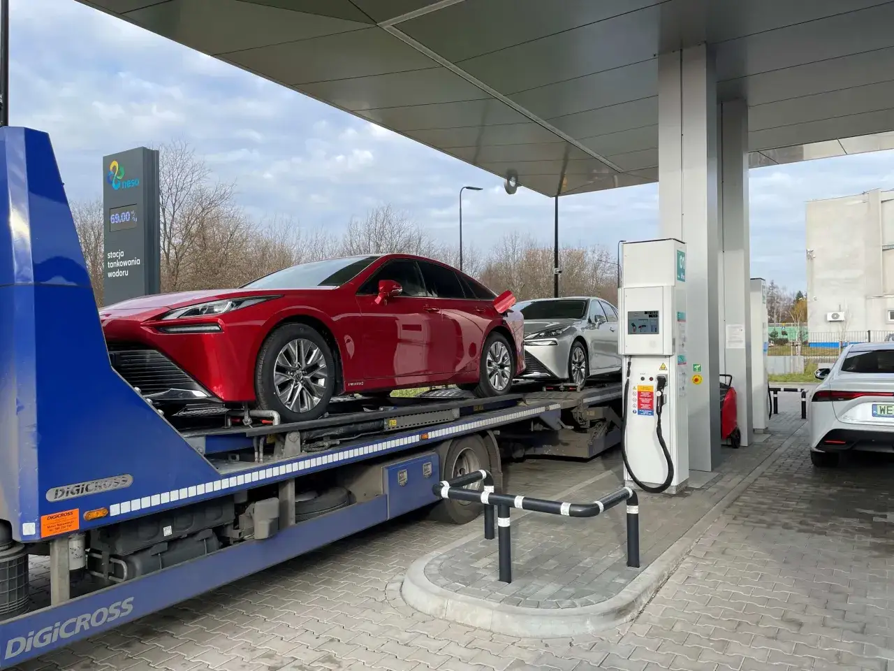 Nowe auta na wodór czekają na tankowanie na stacji Neso. Czerwony sedan na lawecie i srebrny samochód obok.