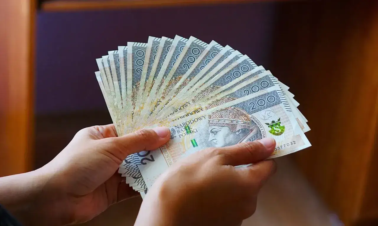 Dwie ręce trzymają wachlarz banknotów 200 zł. Zastanawiasz się, co jeśli nie stać mnie na wymianę pieca?
