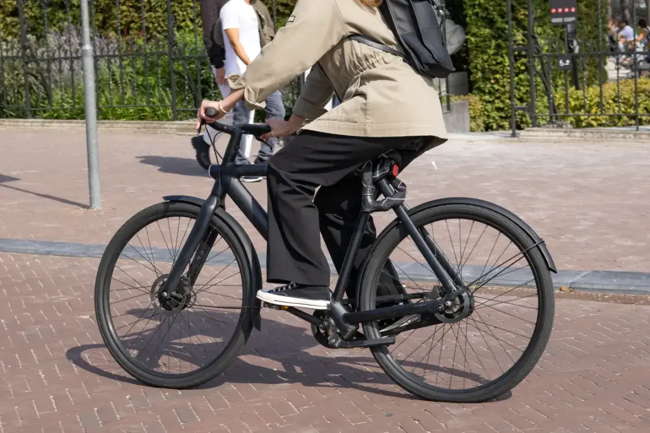 Osoba na czarnym rowerze elektrycznym, który można kupić z dofinansowaniem. Jazda po bruku w słoneczny dzień.