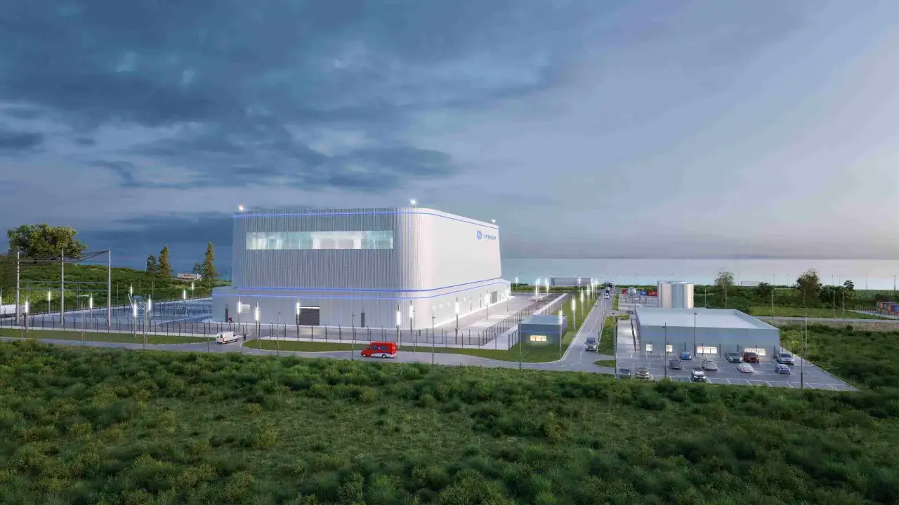 Nowoczesny reaktor SMR Hitachi, otoczony zielenią i infrastrukturą, z widokiem na morze.