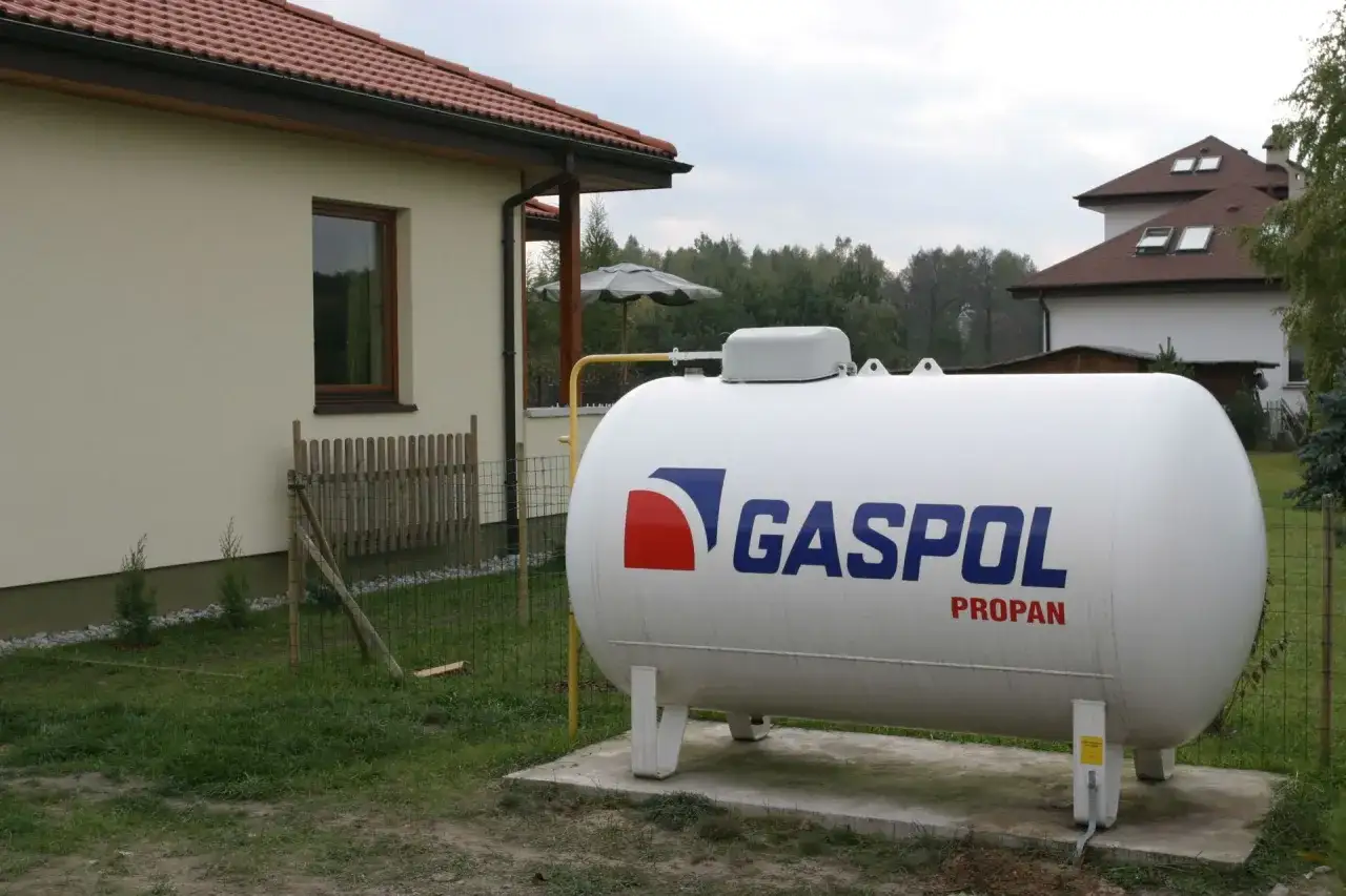 Zbiornik z napisem GASPOL PROPAN, który jest odpowiedzią na pytanie: jaki gaz do ogrzewania domu. W tle dom i drzewa.