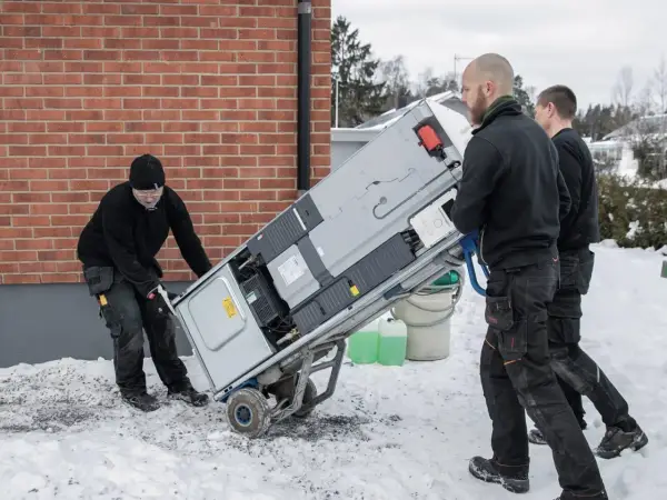 Trzech mężczyzn transportuje nowy piec na wózku. Wymiana pieca w zachodniopomorskim może być konieczna przed zimą.